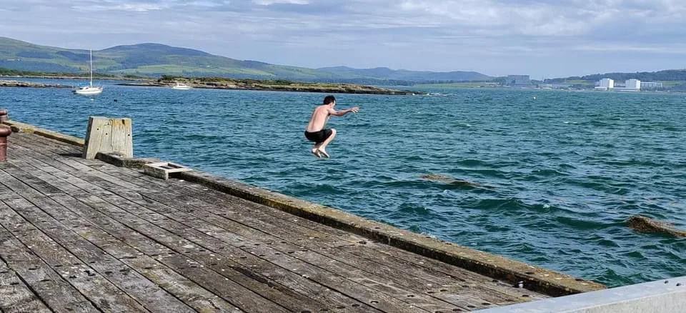Connor mid-jump off a wooden pier into the sea.